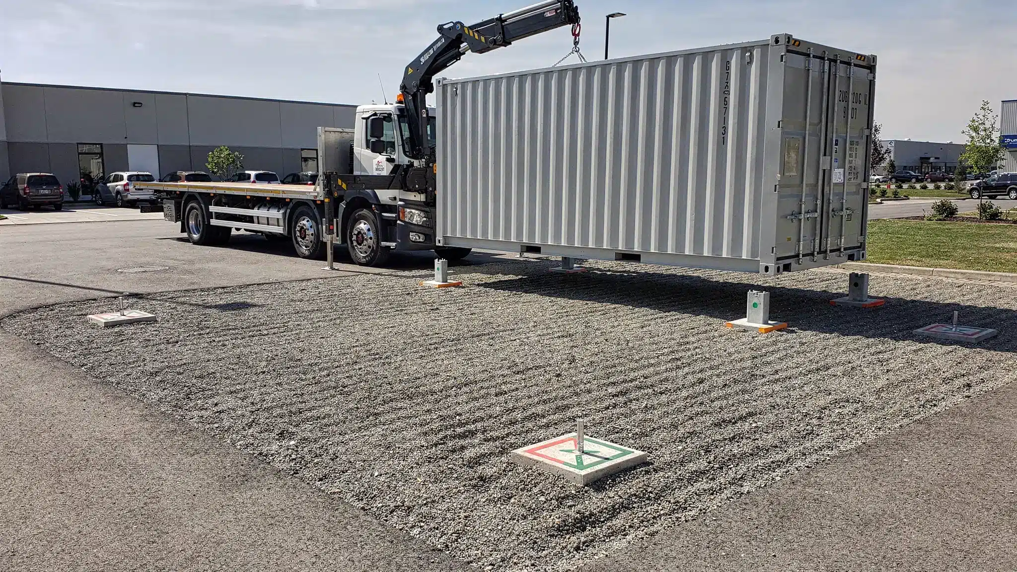 How to Find Shipping Containers for Sale Nearby A clean shipping container being placed on a level gravel pad at a commercial property, with clear driveway access, open space for the delivery truck, and marked corner support points.