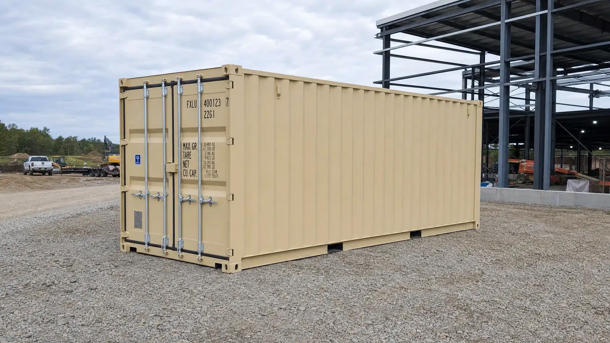A 20ft shipping container resting on a compacted gravel pad beside a commercial job site, with clear truck access and level ground visible around the drop area.