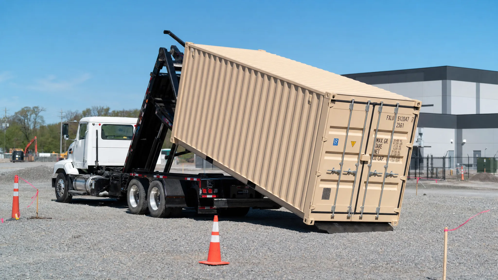 Choosing a Container Delivery Service Without Overpaying A tilt-bed truck sliding a steel shipping container onto a level gravel pad beside a commercial jobsite, with clear access, marked corners, and no overhead obstructions.