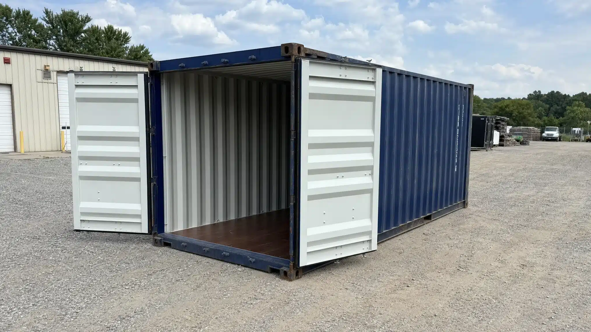 A used 20ft shipping container at a commercial property in Raleigh, shown from a slightly elevated side angle with the doors open and the clean interior floor visible, level on a compacted gravel pad with clear delivery access around it.