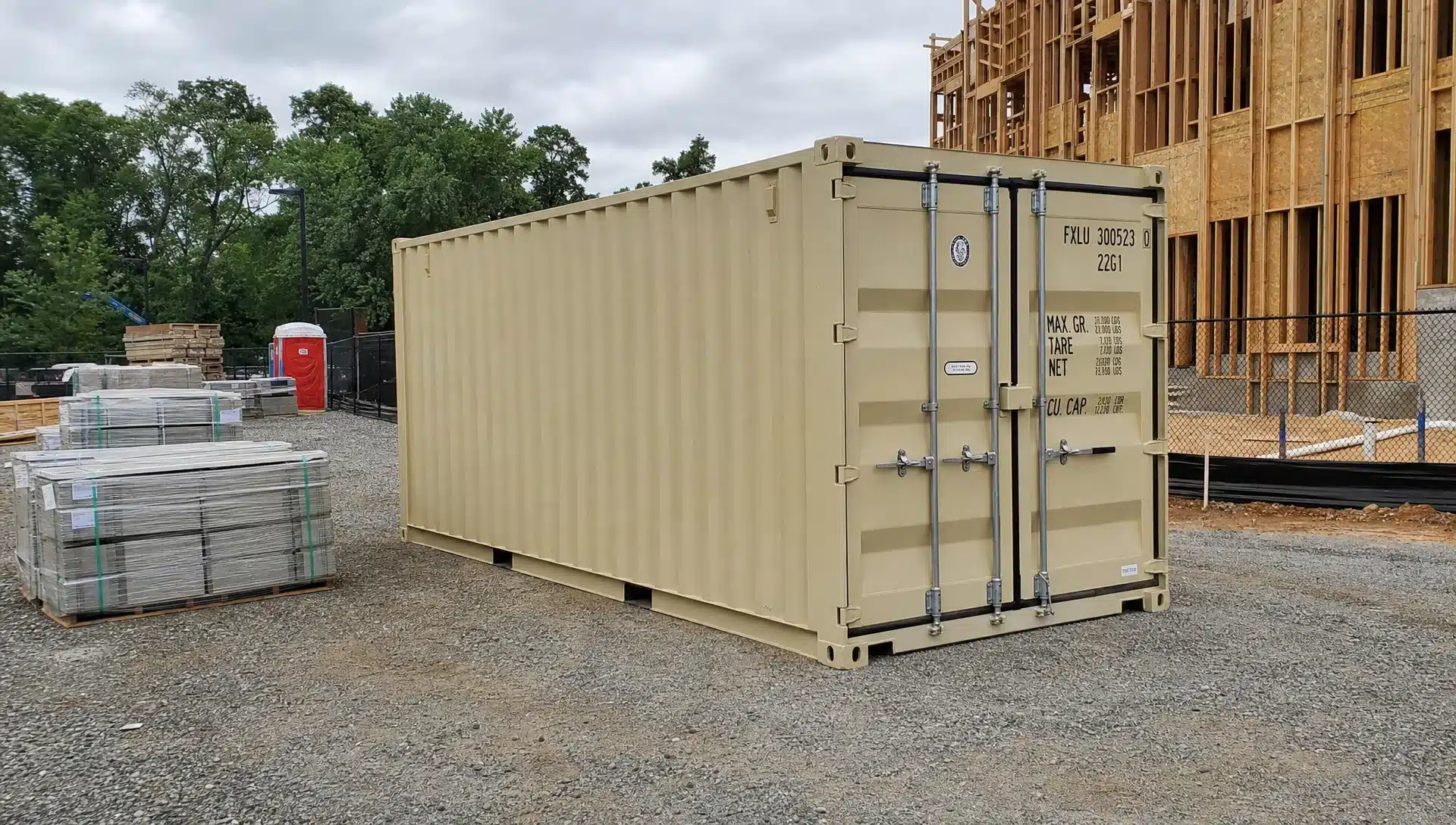 A 20-foot shipping container set on a compacted gravel pad at a Raleigh construction site, with palletized building materials staged nearby and clear delivery access around the unit.