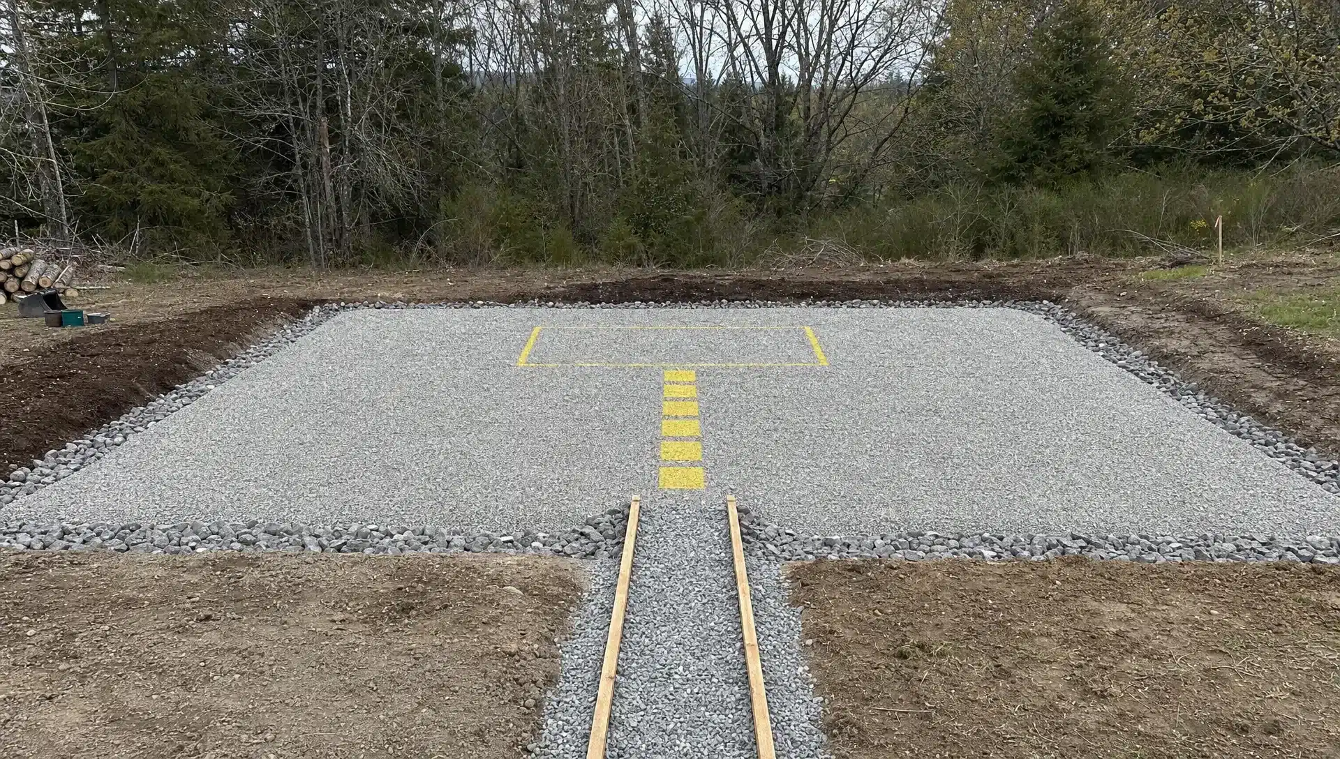 A level gravel pad prepared for a shipping container office, with clear access for delivery equipment, drainage around the perimeter, and a marked entry path leading to the planned office door location.